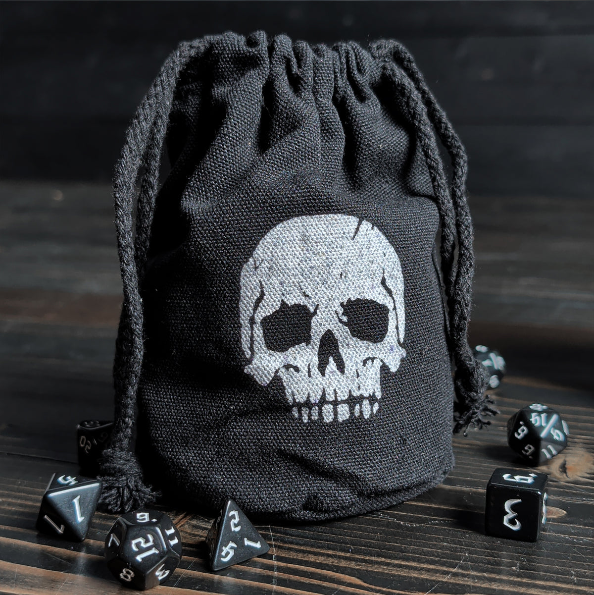 Black dice bag with skull design on a wooden surface with dice around it.