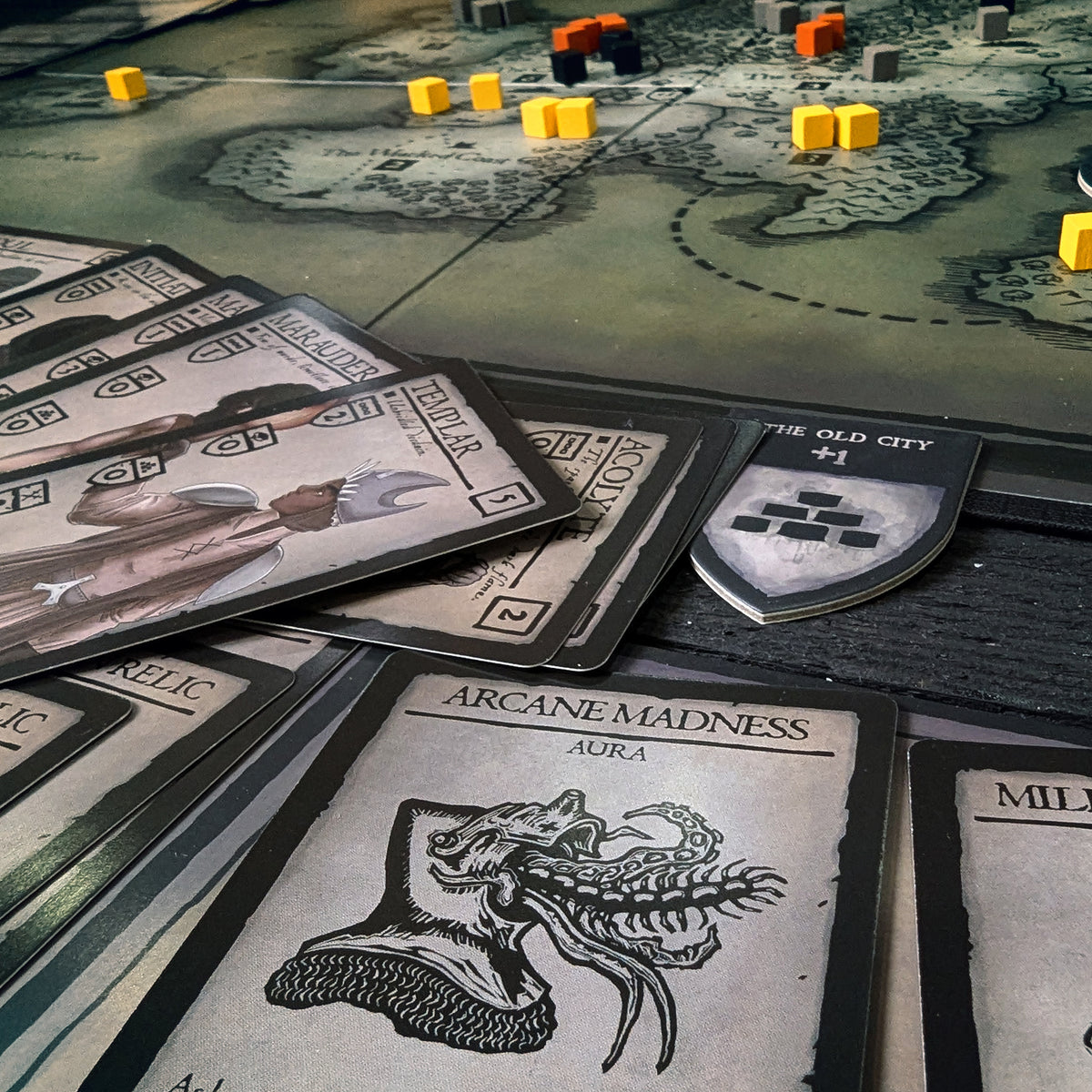 The aura card, "Arcane Madness" on display with a player's hand and captured token from the "Old City"