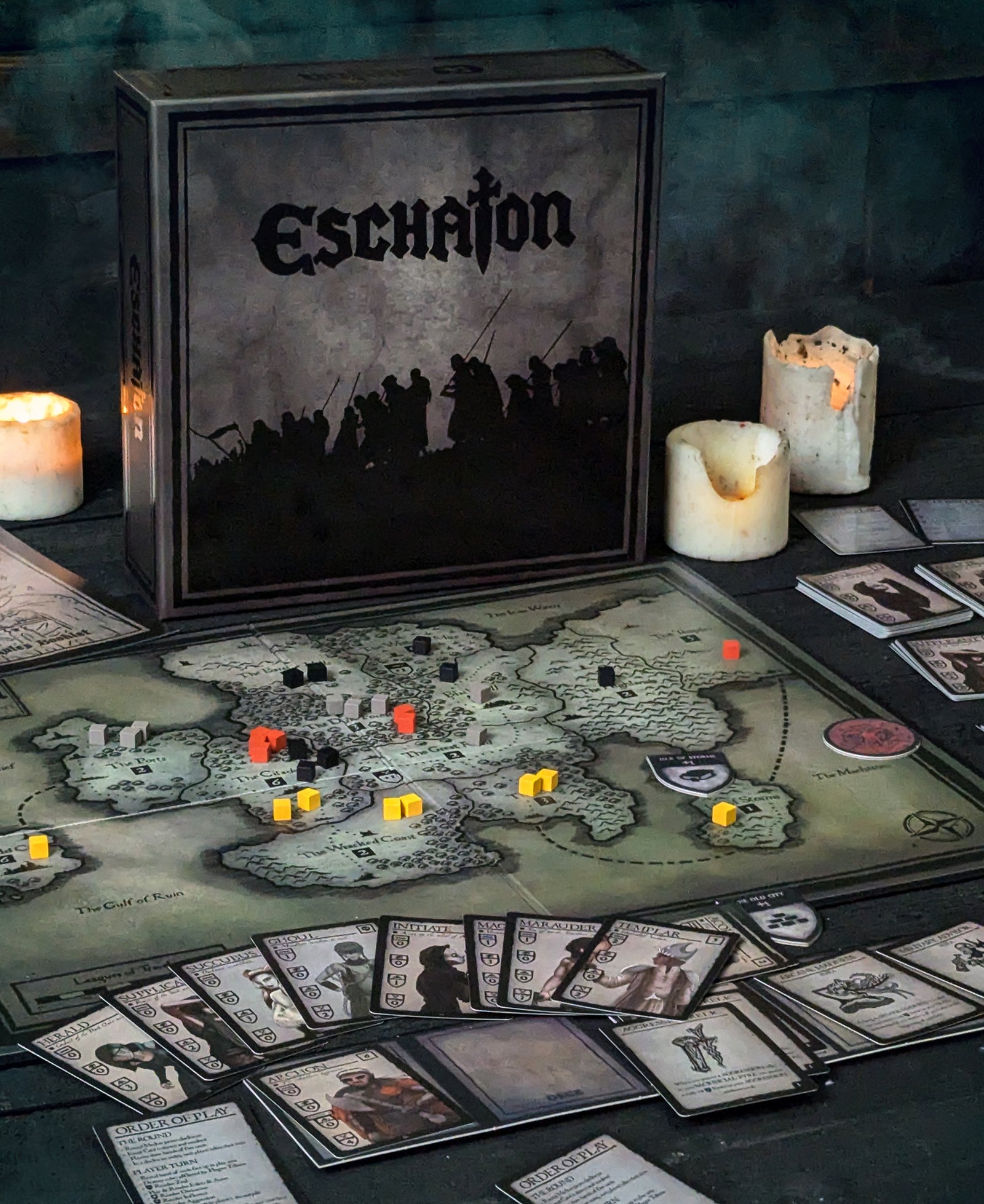 Eschaton board game box displayed beside a realm map on a tabletop, with cultist cards in play and candles glowing in the background.