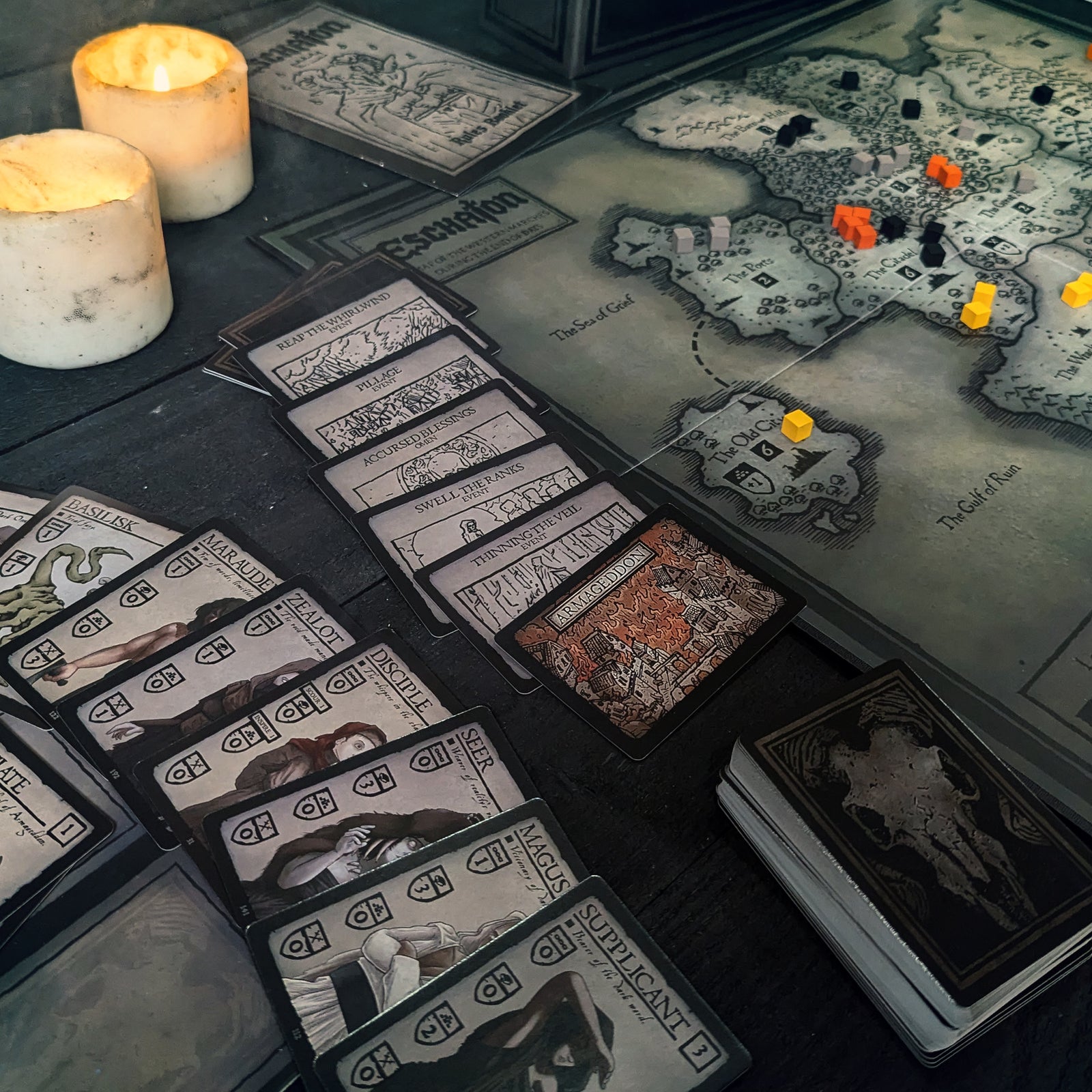 Eschaton event cards and the Armageddon card laid beside the game board, which displays a detailed map of the Accursed Realm.